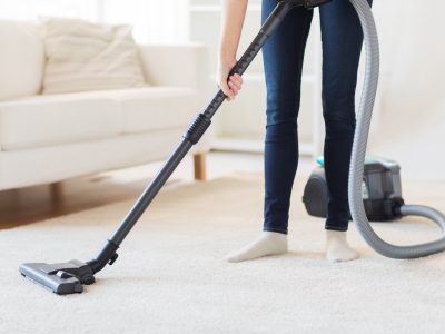 people, housework and housekeeping concept - close up of woman with legs vacuum cleaner cleaning carpet at home