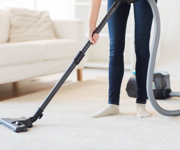 people, housework and housekeeping concept - close up of woman with legs vacuum cleaner cleaning carpet at home